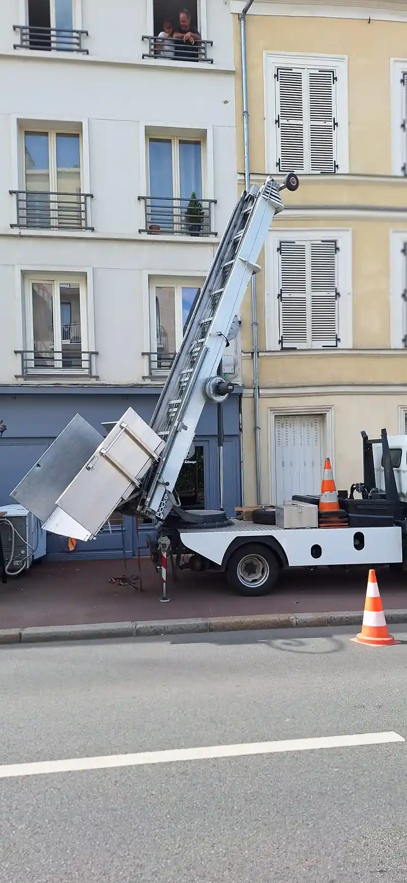 Monte-meuble installé devant un immeuble, avec des personnes visibles.