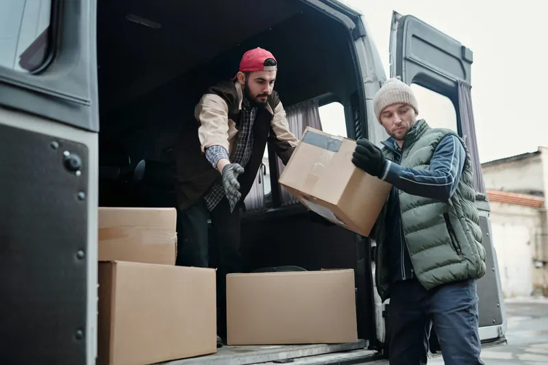 Deux personnes déplacent un carton près d’un fourgon.