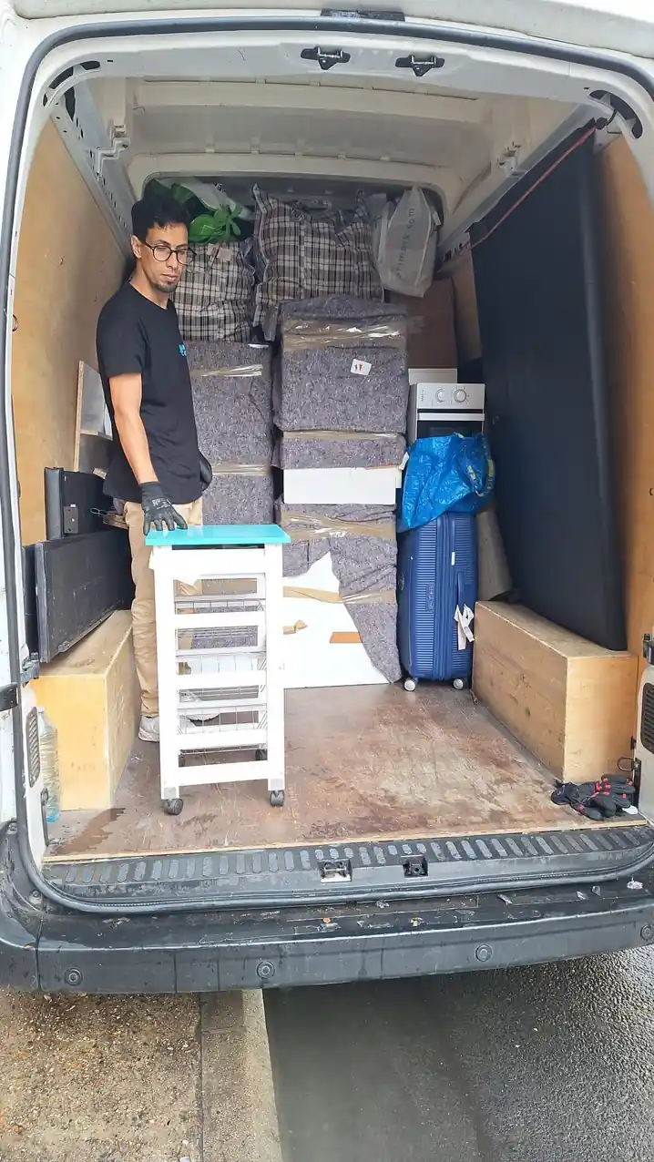 Personne tenant un petit meuble près d’un véhicule chargé.
